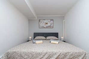 A bedroom with a large bed, two bedside tables, a wall-mounted artwork, and a door. - Apartment Aurora (Opatija)