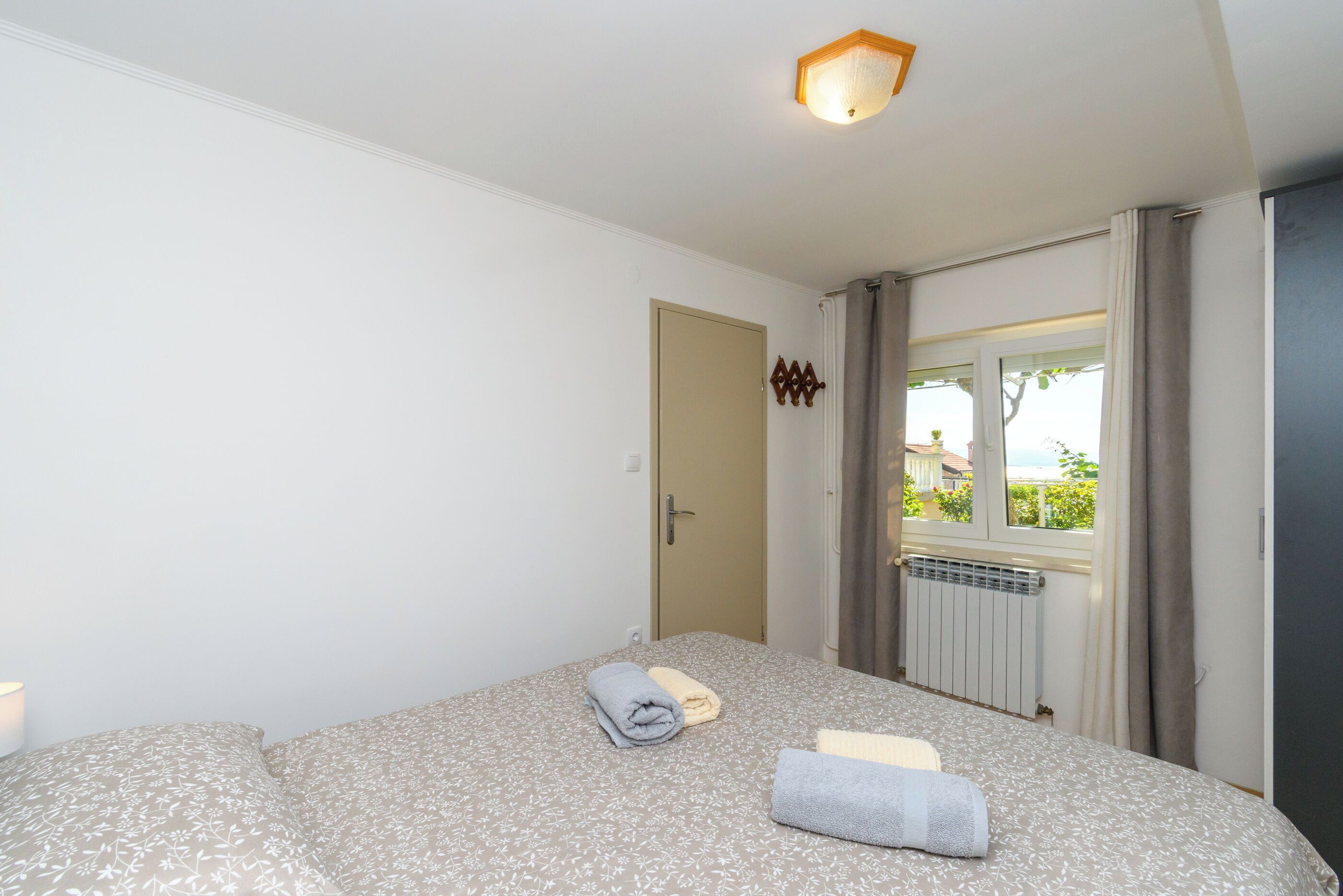A bedroom with a bed, a radiator, a window with curtains, and a door.
