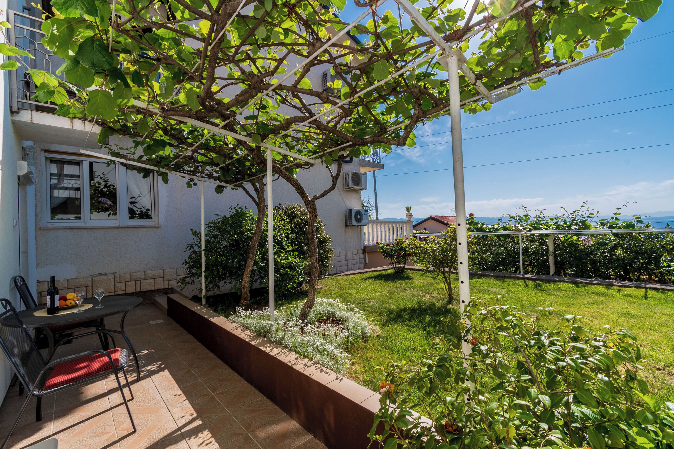 Una veranda con tavolo e sedie, un pergolato e vista su giardino e edificio.