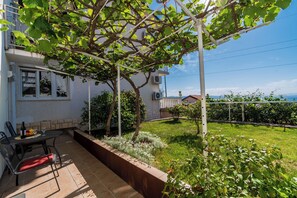A patio with a table and chairs, a pergola, and a view of a garden and building. - Apartment Aurora (Opatija)