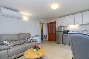 A living room with a sofa, a round coffee table with flowers, a remote control, and a kitchen with appliances. - Apartment Aurora (Opatija)