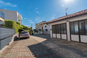 A residential street with a car parked on the side, a house with a tiled roof, and a clear blue sky. - Apartment Aurora (Opatija)