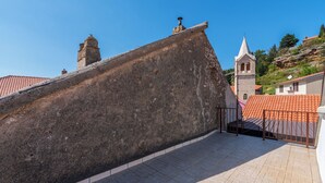Un muro de piedra con barandilla de metal, tejado de baldosas y una torre de iglesia al fondo.