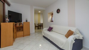 Una sala de estar con un sofá, televisor, aparador de madera y un comedor al fondo.