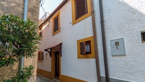Un callejón estrecho con un edificio de fachada blanca, detalles amarillos y contraventanas de madera.