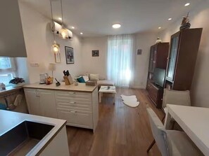 Eine moderne Küche mit weißen Schränken, einer zentralen Kochinsel, Pendelleuchten und einem Essbereich mit weißem Tisch und Stühlen.