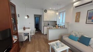 Ett kompakt bostadsutrymme med ett litet kök, en matplats och en soffa med ett mönstrat överkast.