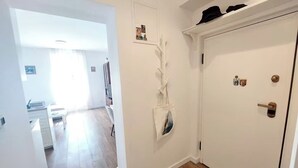 En hall med en vit dörr, en liten hylla med hattar och en väggdekoration.