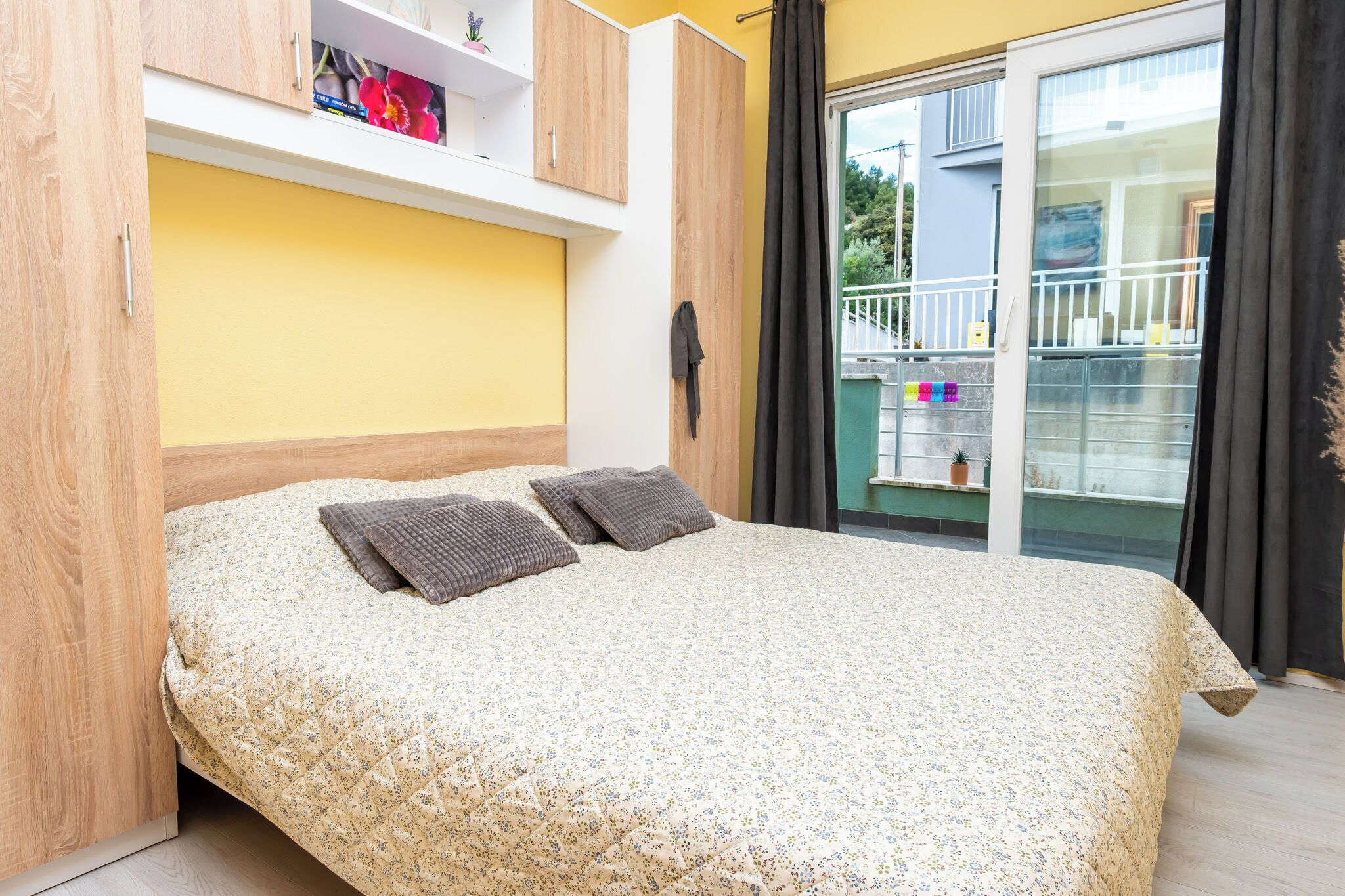A bedroom with a bed, wooden wardrobe, and a view of the outside.
