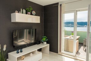 Ein modernes Wohnzimmer mit einem Flachbildfernseher, einem weißen Konsolentisch und einem Balkon mit Blick auf eine Brücke und Hügel.