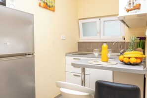 Eine kleine Küche mit Kühlschrank, Spüle, Arbeitsplatte und einem Stuhl.