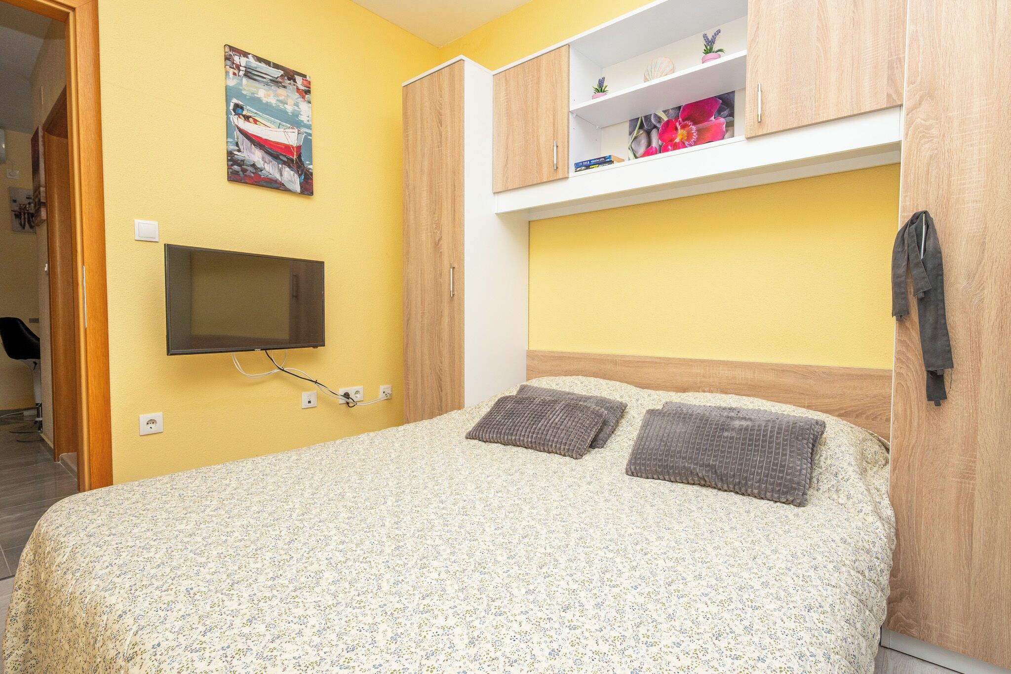 A bedroom with a bed, a mounted TV, wooden cabinets, and a painting on the wall.