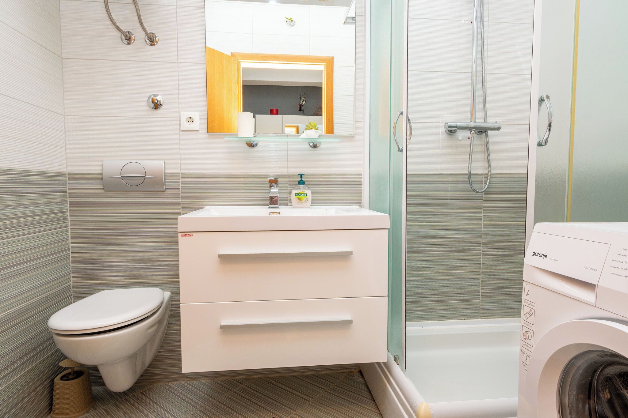 Une salle de bain moderne équipée de toilettes, d’un lavabo, d’un miroir, d’une douche et d’un lave-linge.