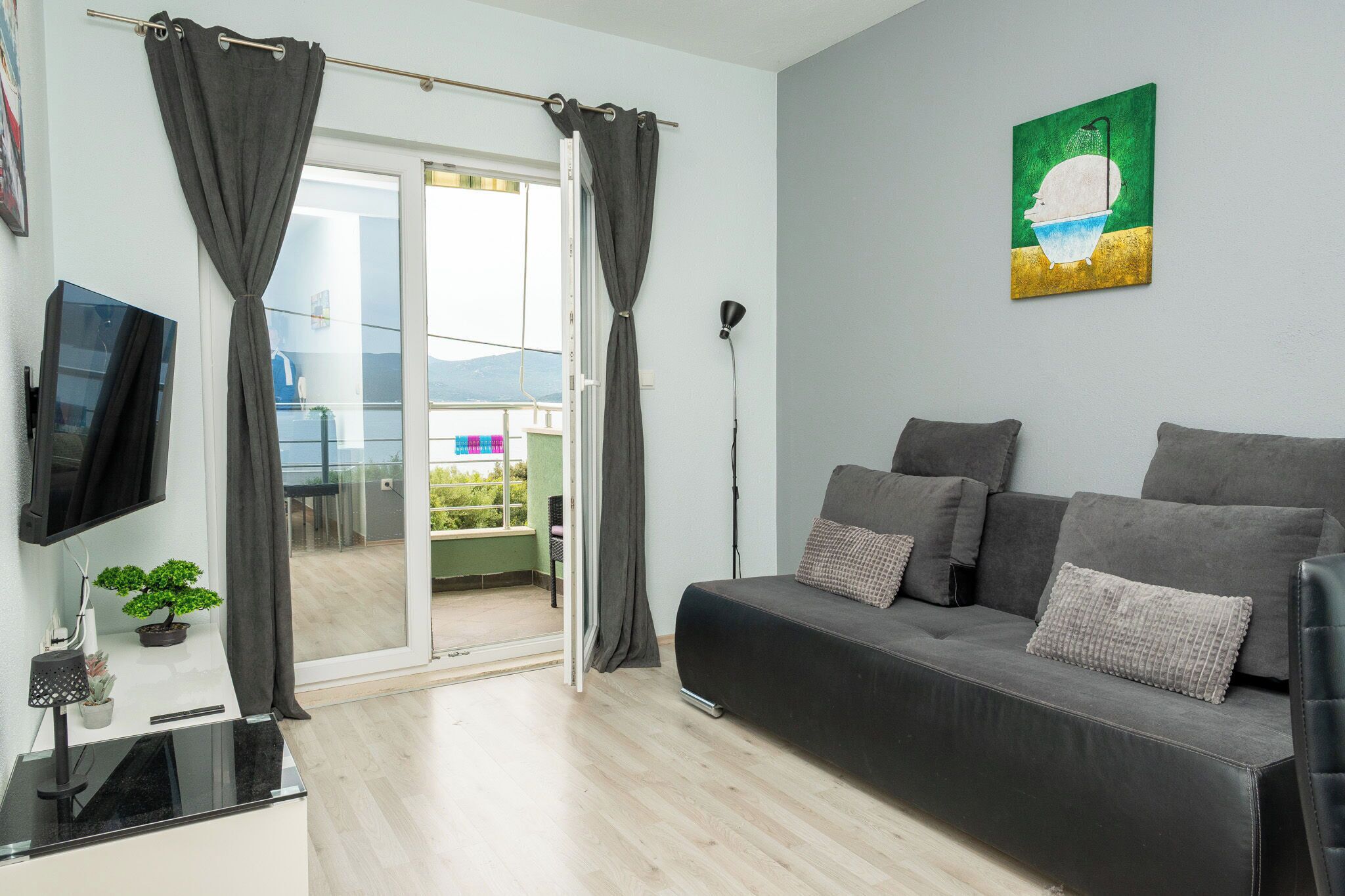 A modern living room with a sofa, a flat-screen TV, a potted plant, and a sliding glass door leading to a balcony.