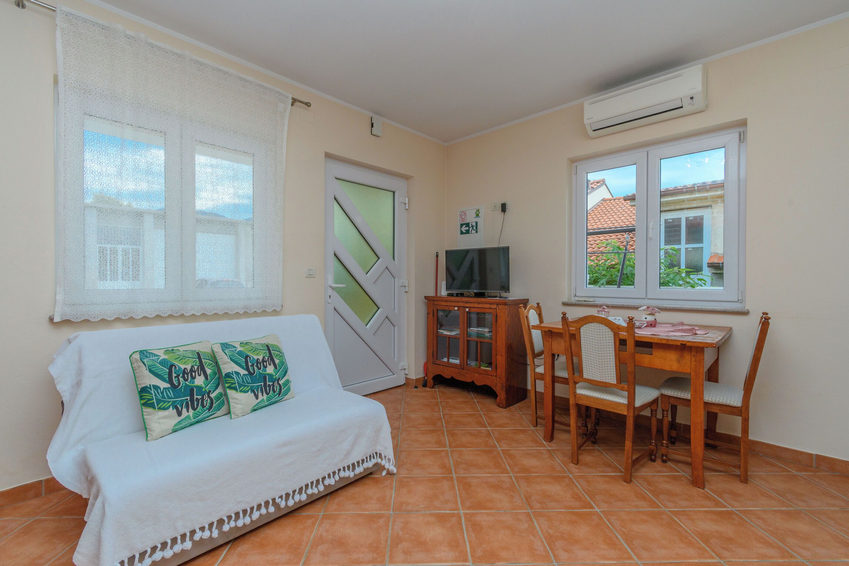 A room with a sofa, a TV on a stand, a dining table with chairs, and a window with a view.