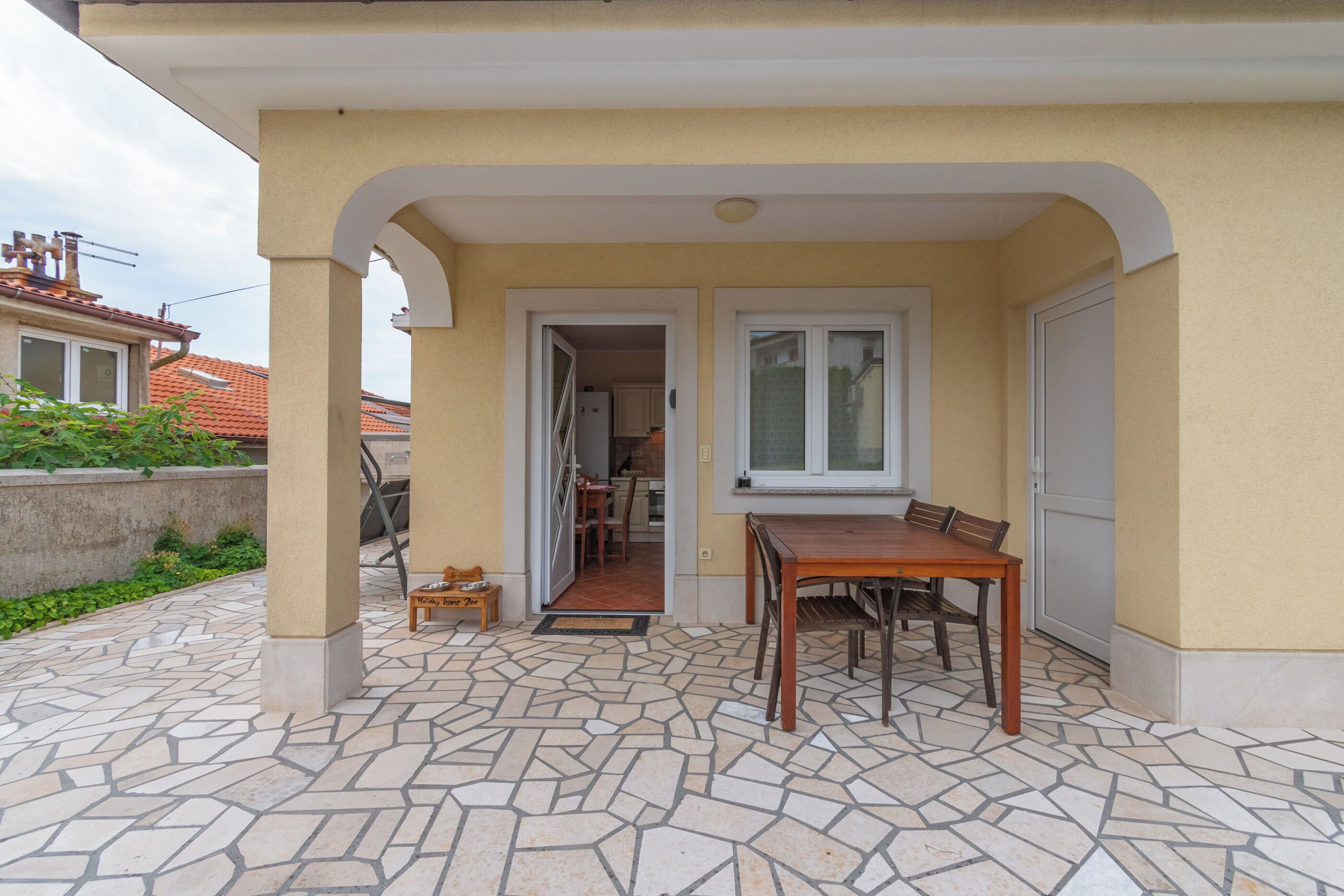 A covered outdoor patio with a tiled floor, a wooden table, and chairs.