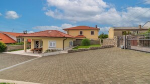 A residential area with paved driveways, a small patio with a table and chairs, and a stone wall. - House Holiday Home Zoe (Kraljevica)