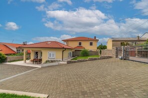 Un área residencial con entradas pavimentadas, un pequeño patio con mesa y sillas, y un muro de piedra.