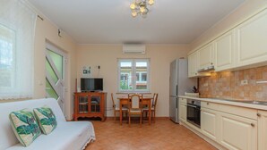 A compact kitchen with a dining area, a sofa with decorative pillows, and a television. - House Holiday Home Zoe (Kraljevica)