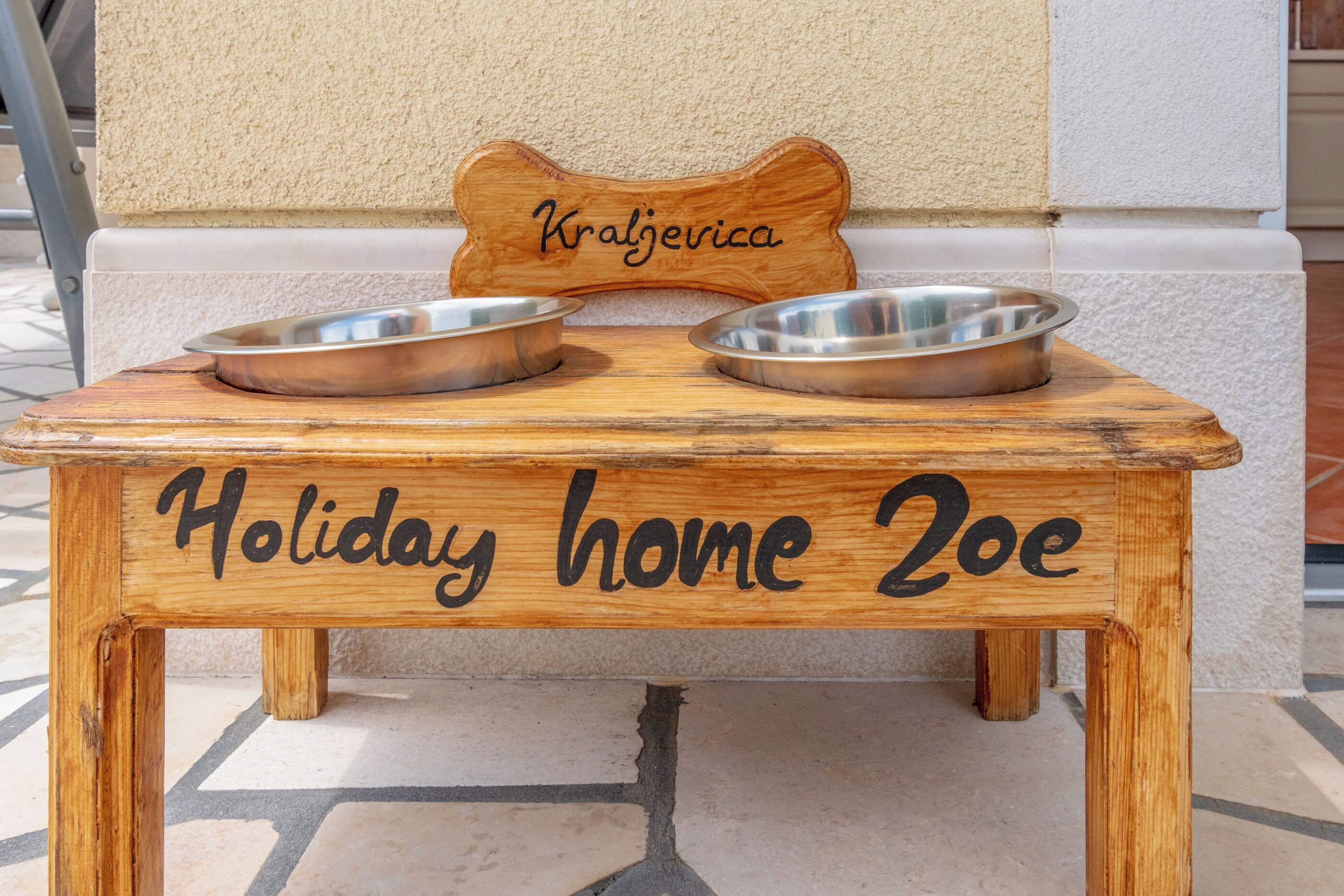A wooden pet feeding station with two metal bowls and a nameplate reading 'Kraljerica.'