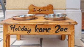 A wooden pet feeding station with two metal bowls and a nameplate reading 'Kraljerica.'