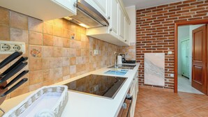A kitchen with a modern stove, white cabinets, and a brick wall. - House Holiday Home Zoe (Kraljevica)