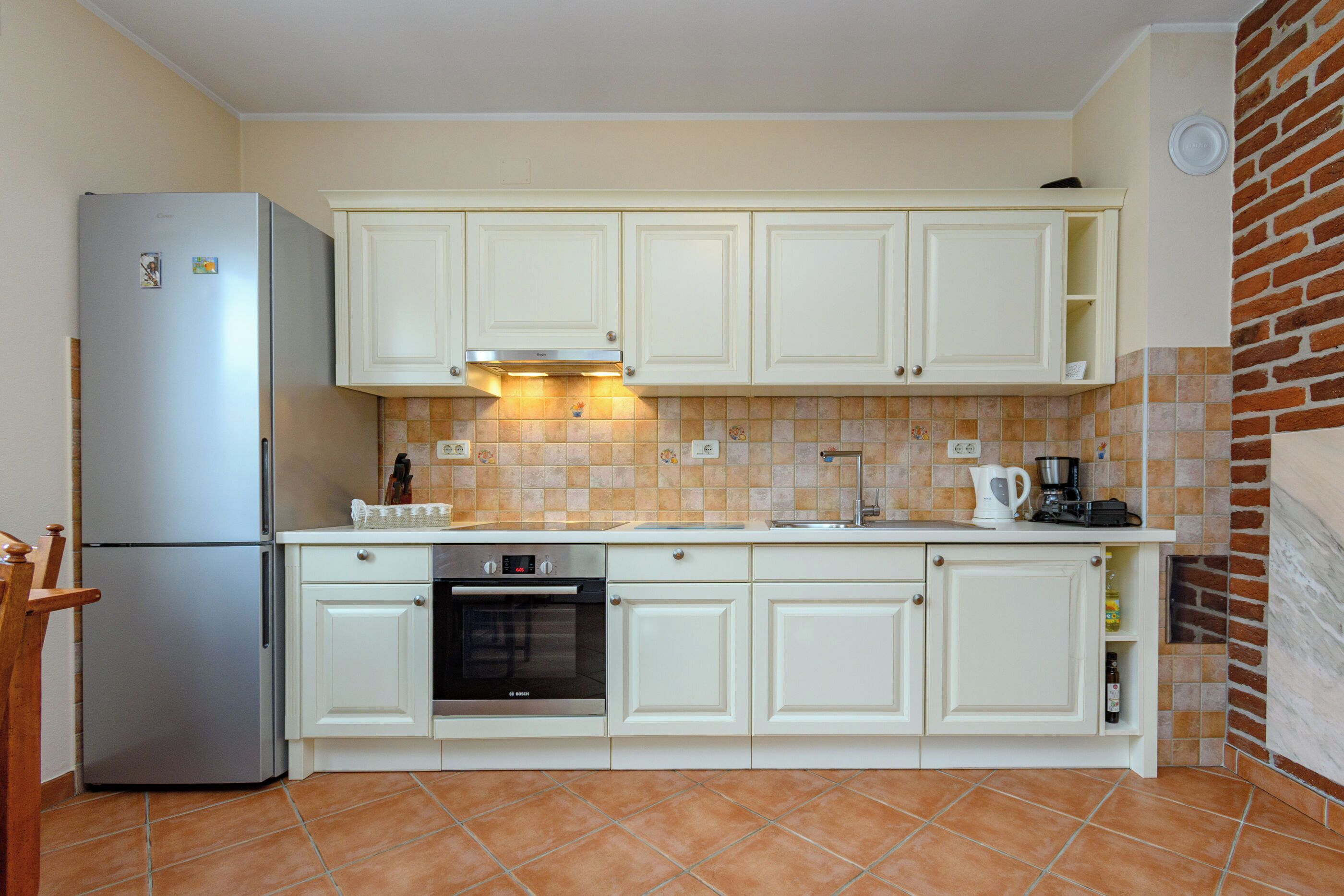 Una cocina con armarios blancos, un refrigerador de acero inoxidable, un horno y un salpicadero de azulejos.
