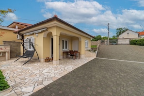 Ein Haus mit einer gefliesten Terrasse, einem überdachten Sitzbereich im Freien und einer Steinmauer.