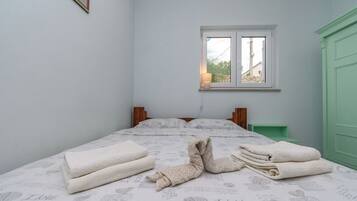 A neatly made bed with folded towels, a window with a view, and a green door.