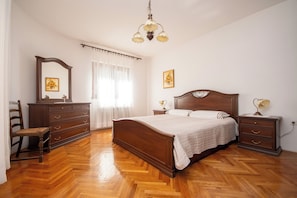 Ein Schlafzimmer mit einem hölzernen Bett, einem Nachttisch, einer Kommode, einem Stuhl und einer Pendelleuchte.