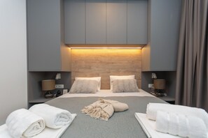 Ein modernes Hotelzimmer mit einem großen Bett, zwei Nachttischen, einem Kopfteil mit integrierter Beleuchtung und Blick ins Zimmerinnere.