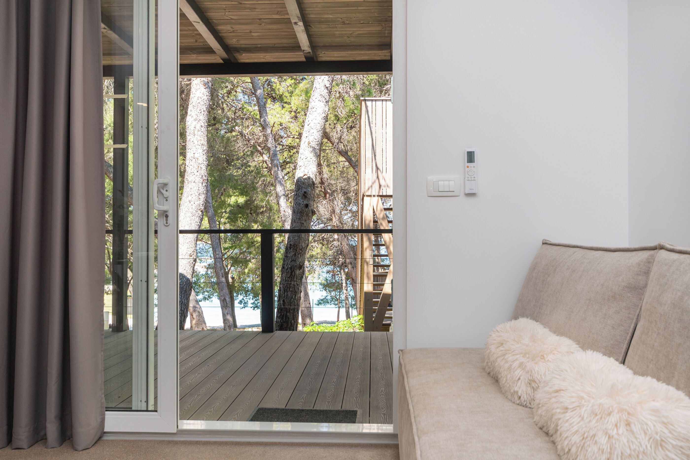 Une pièce dotée d’une porte-fenêtre coulissante donnant sur une terrasse, d’un canapé avec des coussins moelleux et d’un thermostat fixé au mur.