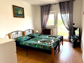 A bedroom with a bed, a desk with a computer, a window with curtains, and a painting on the wall. - House House Lola (Rasa)