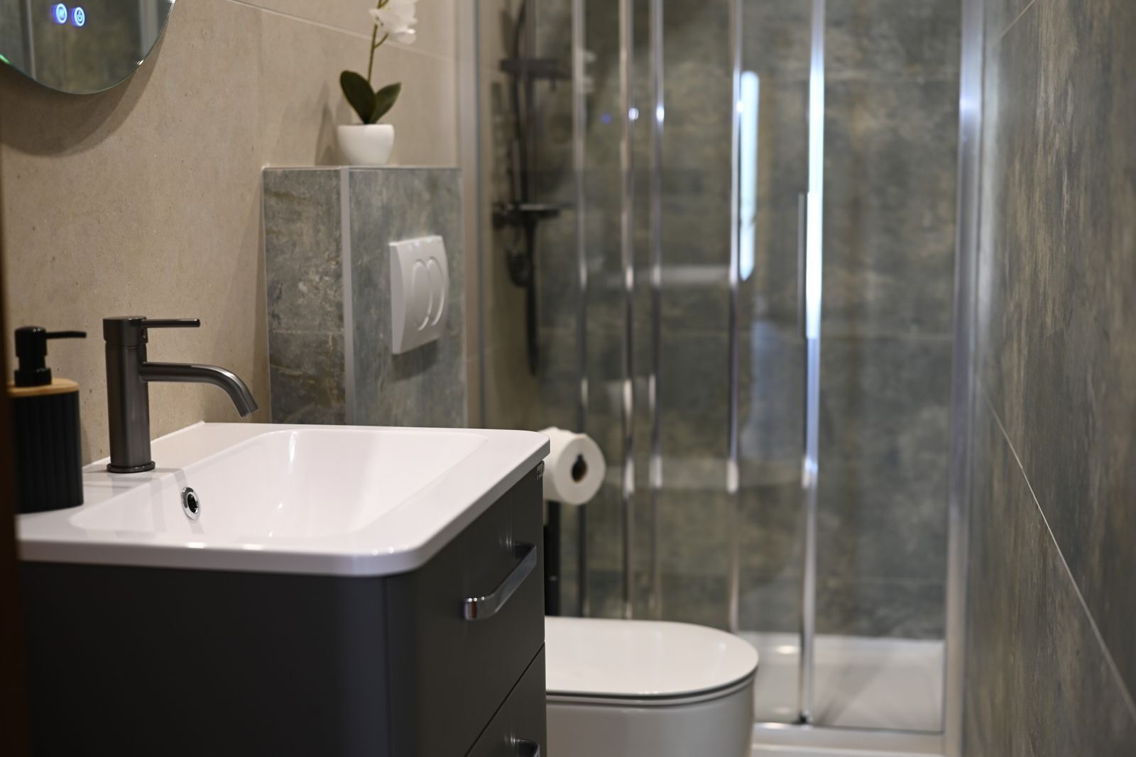 A modern bathroom with a white sink, black faucet, and a glass shower enclosure.