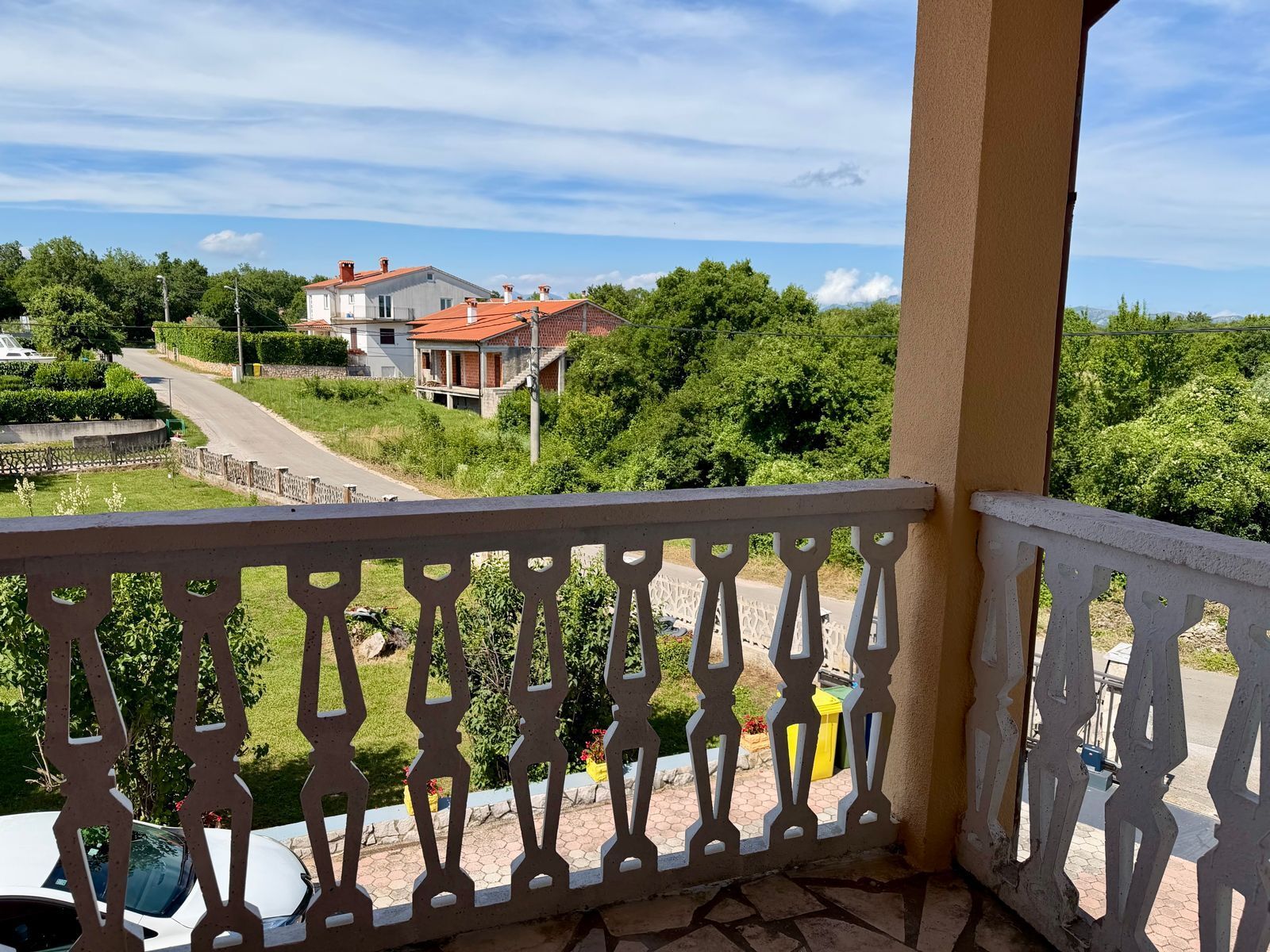 A balcony with a white balustrade overlooking a residential street with houses and greenery.