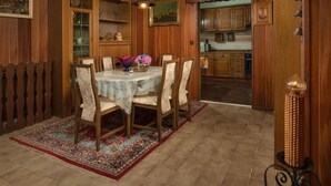 A dining area with a round table, chairs, a rug, wooden cabinets, and a kitchen in the background. - House House Lola (Rasa)