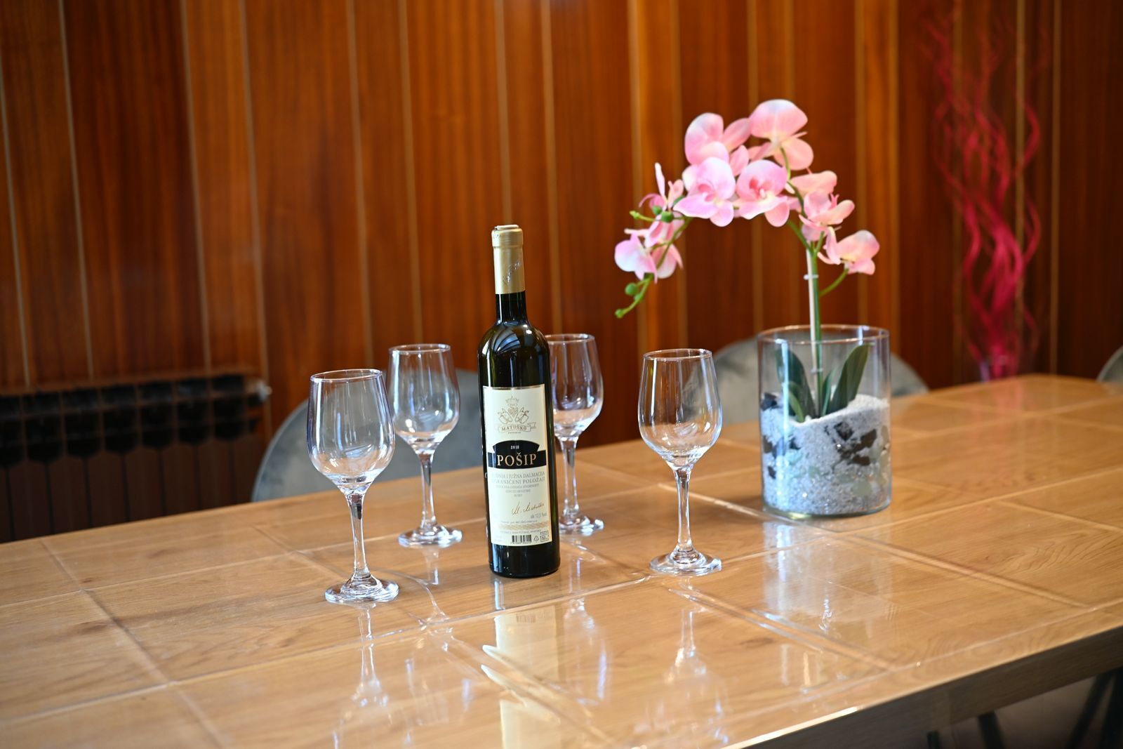 A table with a bottle of wine, empty wine glasses, and a vase with pink flowers.