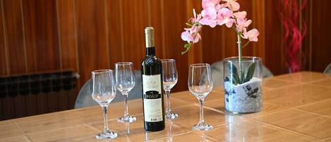 A table with a bottle of wine, empty wine glasses, and a vase with pink flowers.