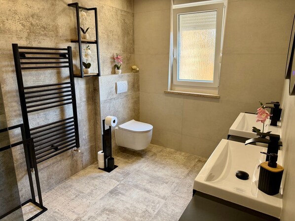 A bathroom with a toilet, a towel rack, a sink, and a window. - House House Lola (Rasa)