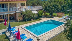 A pool with lounge chairs and umbrellas, a stone pool deck, and a house with a balcony. - House House Lola (Rasa)