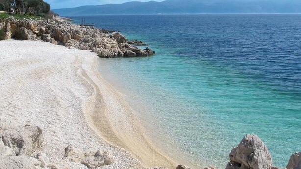 A beach with clear water, rocky shoreline, and distant mountains. - House House Lola (Rasa)