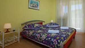 A bed with floral bedding, a bedside table with a lamp, and a painting on the wall. - House House Lola (Rasa)
