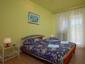 A bed with floral bedding, a bedside table with a lamp, and a painting on the wall. - House House Lola (Rasa)