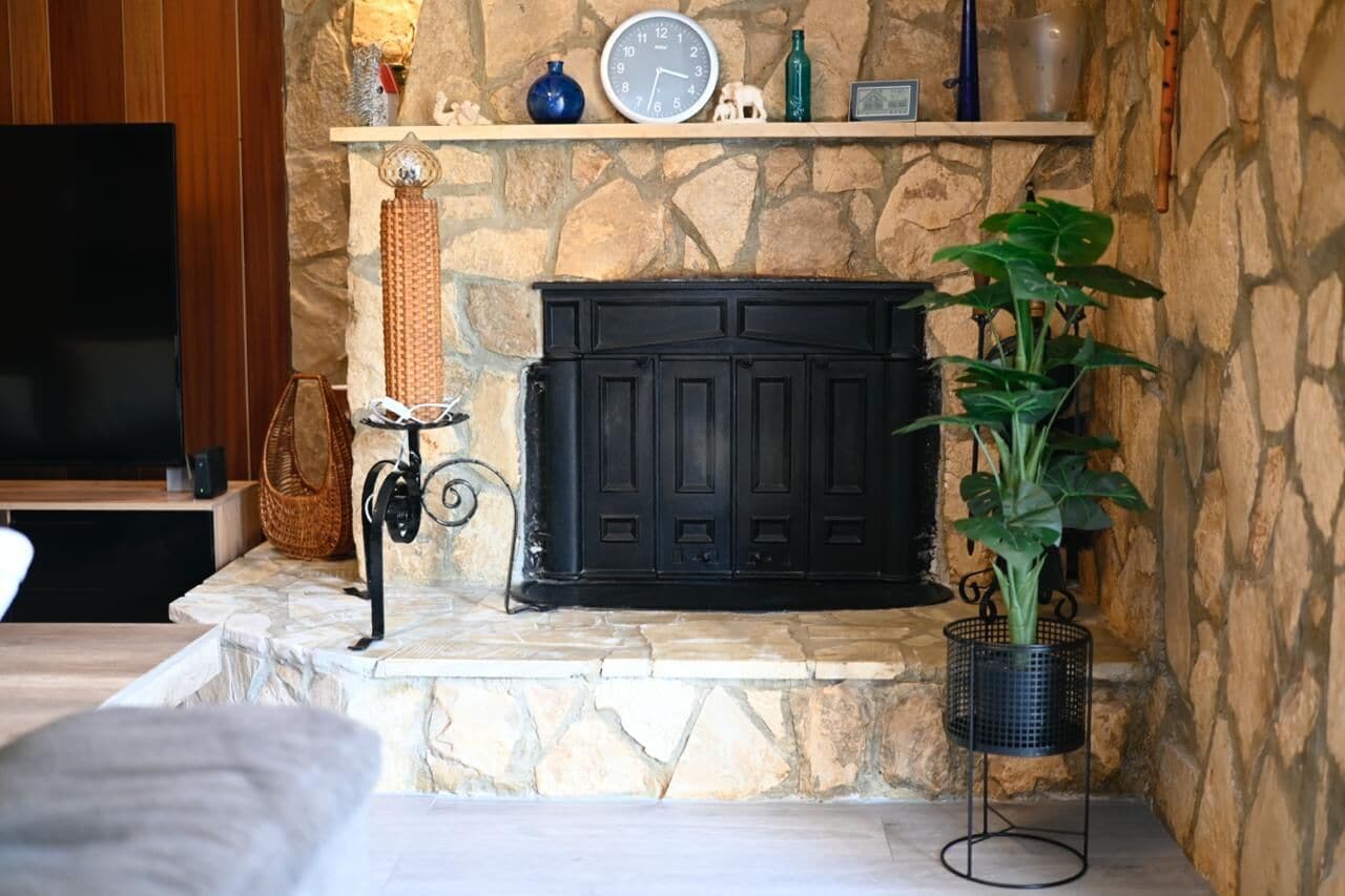 A stone fireplace with a clock above it, a television to the left, and a potted plant to the right.