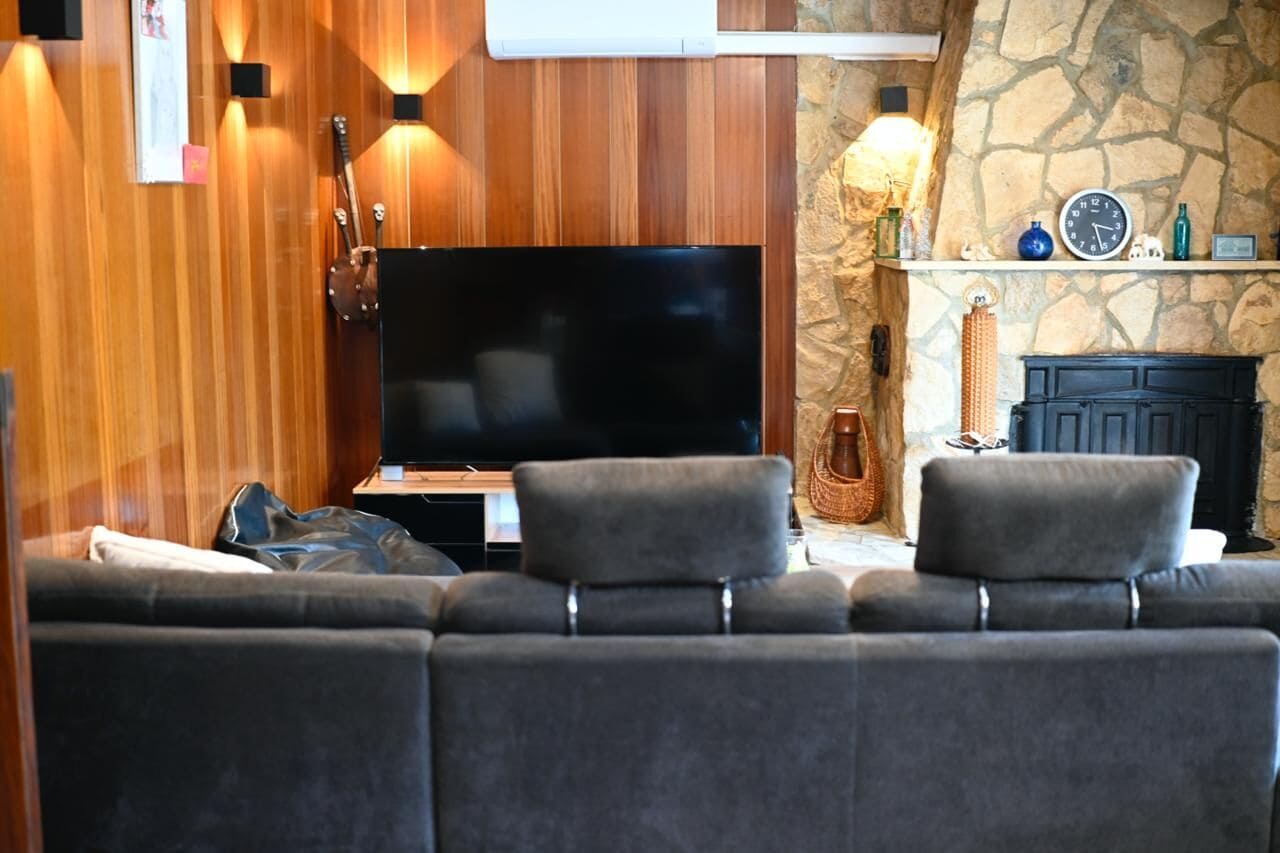 A living room with a flat-screen TV, a stone fireplace, and a wooden wall.