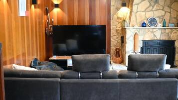 A living room with a flat-screen TV, a stone fireplace, and a wooden wall.
