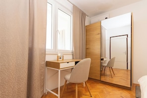 Ein Schlafzimmer mit Holzschreibtisch, Stuhl, Bett, Kleiderschrank und Spiegel.