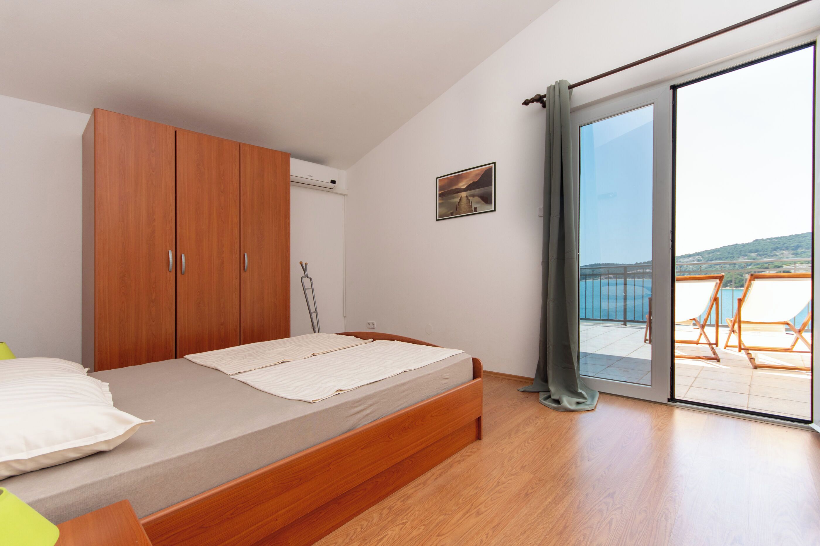 Ein Schlafzimmer mit Bett, Holzschrank und Balkon mit Sitzgelegenheiten.