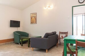Ein Wohnzimmer mit einer Couch, einem an der Wand montierten Fernseher, einem Gemälde und einem Essbereich mit Tisch und Stühlen.