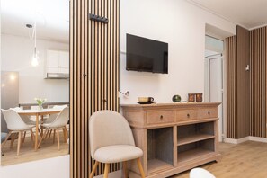 Ein modernes Wohnzimmer mit Fernseher, Wandpaneelen aus Holz, Essbereich und einer Couch.
